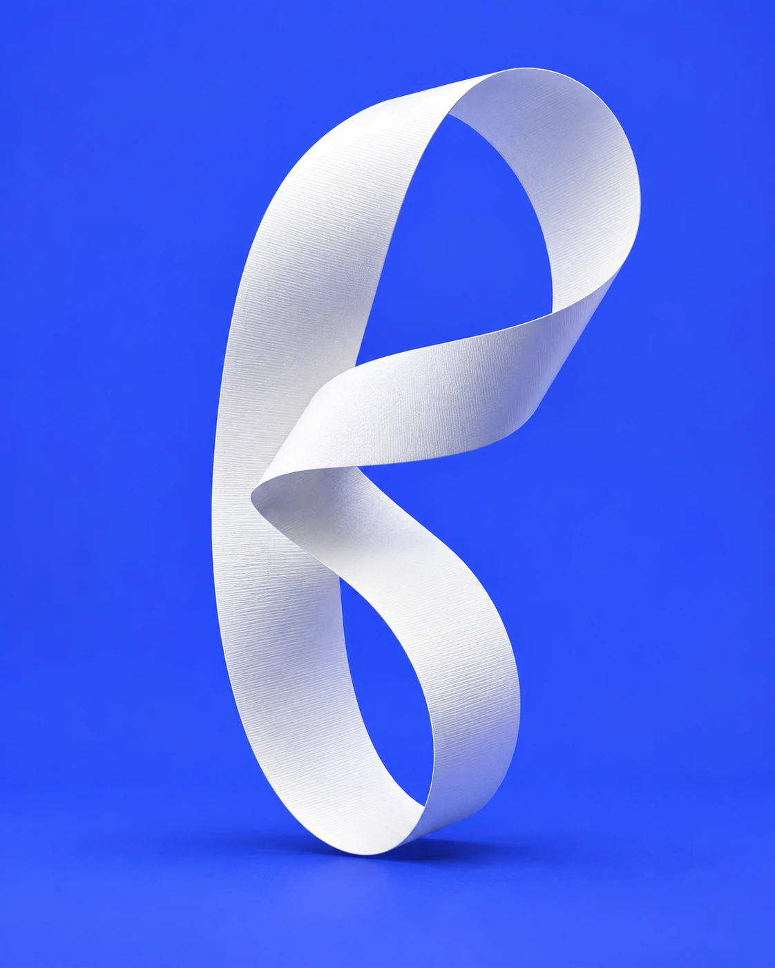 A white paper ribbon folded in a sculptural loop on cobalt blue